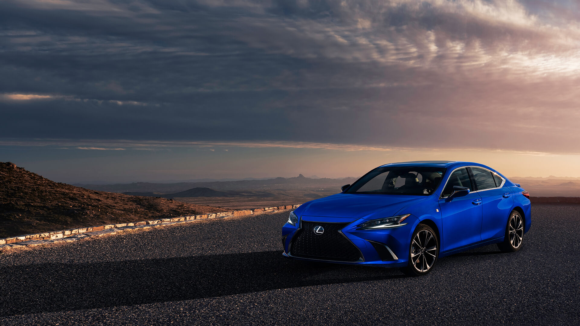 Blue Lexus ES F SPORT is parked on the road next to rocky terrain.